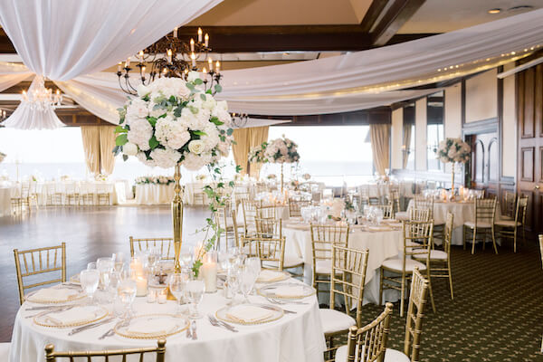 Tampa wedding - Tampa wedding reception - Rusty Pelican Restaurant - Rusty Pelican Restaurant wedding - Rusty Pelican Restaurant wedding reception - gold and white wedding reception - draped ceiling with twinkle lights- gold chiavari chairs - white centerpieces on gold risers - gold beaded glass charger plates