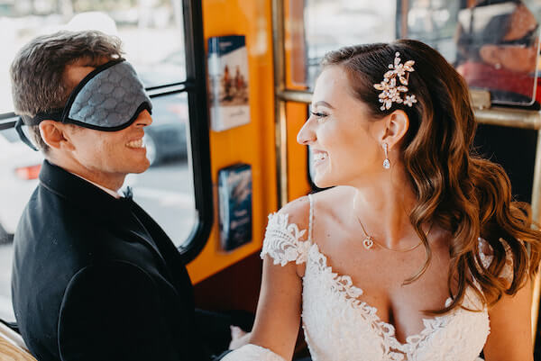 blindfolded groom sitting next to his bride to be on the way to their wedding ceremony