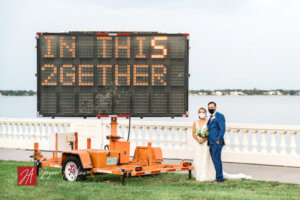 masked Tampa bride and groom standing next to COVID "in this 2gether' sign along the road.