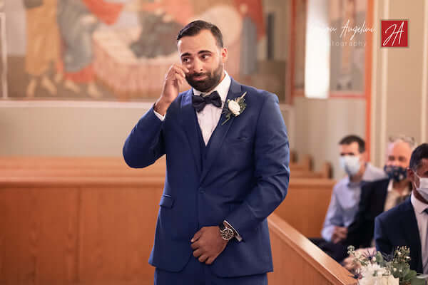 groom crying as socially distant wedding guest wearing mask watch bride's arrival