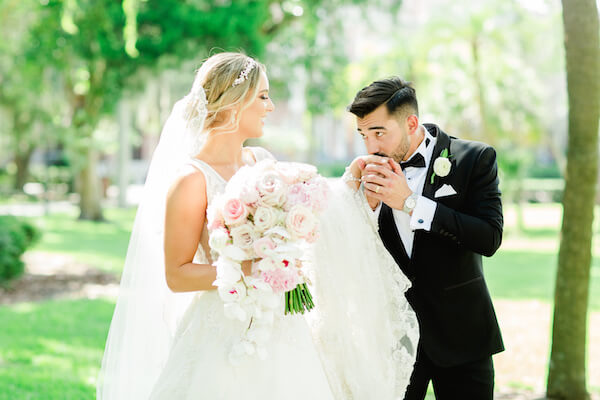 Groom kissing brides hand while walking in a park