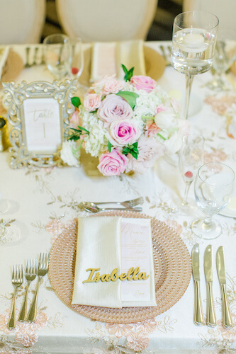 rose gold charger plates on a lace embroidered table cloth with a pink and white floral centerpiece