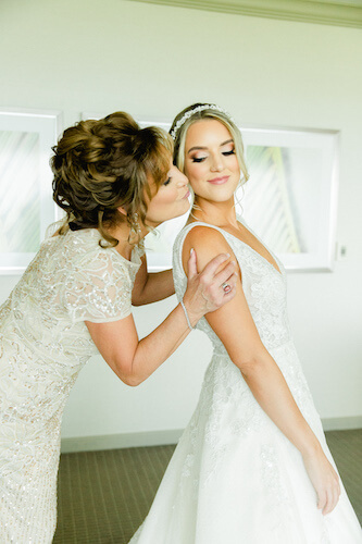 Mother of the bride kissing her daughter on the cheek as she finishes getting dressed