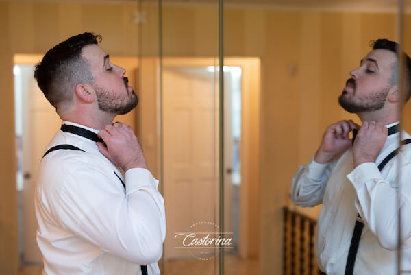 groom standing in front of a mirror adjusting his bow tie