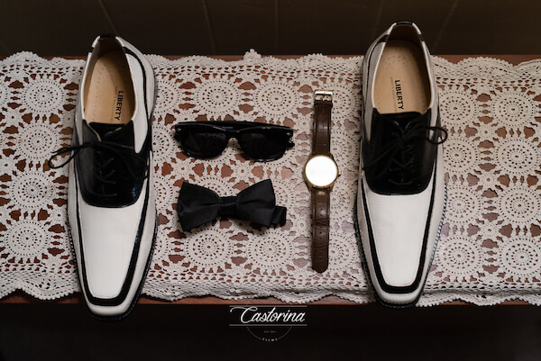 photo of the grooms white shoes with black trim, bow tie, sunglasses and watch