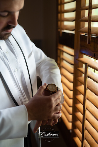 groom in white tuxedo jacket putting on his watch