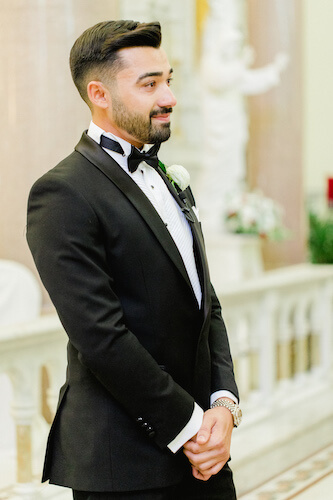 groom wearing a classic black tuxedo with wing tip collar black bow tie and white pocket square