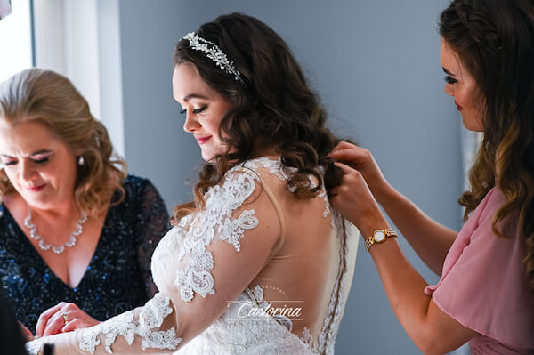 bridesmaid and mother of the bride helping her put on her wedding gown