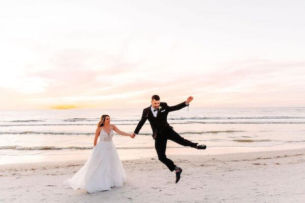 Groom jumping for joy walking on the beach with his bride