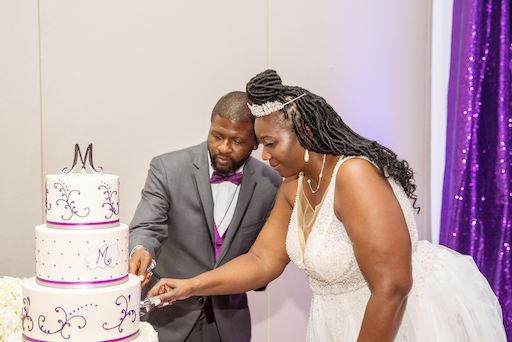 bride and groom cutting their purple and white wedding cake by The Artistic Whisk