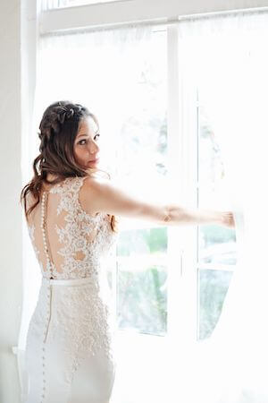 Bride in a lace wedding gown standing at the window