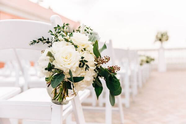 glass vases filled with white flowers on white garden chairs 