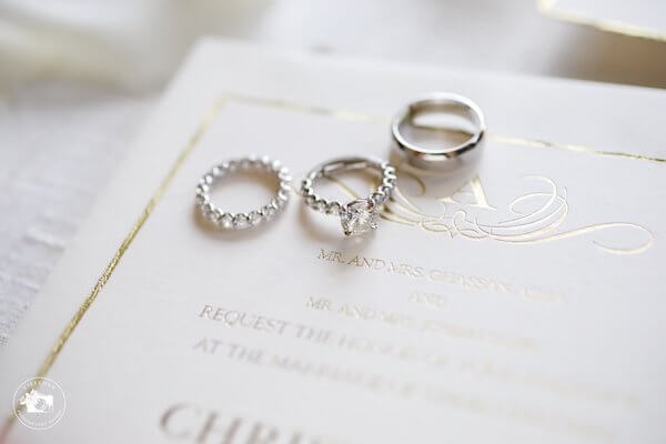 wedding and engagement rings sitting on a white and gold wedding invitation