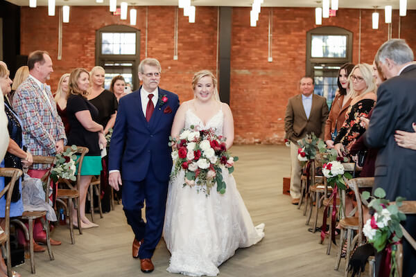 bride smiling as she and her father walk down the aisle to her groom