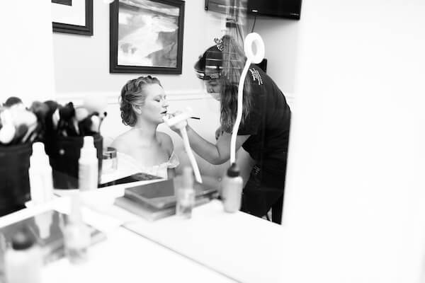 makeup artist wearing a mask and face shield applying bride's makeup