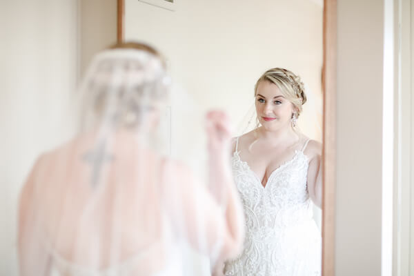 Bride with loose up do and Boho styled wedding gown looking in the mirror