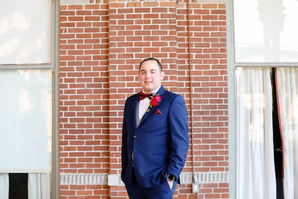 Tampa groom in a navy blue suit with burgundy bow tie and pocket square standing on the front porch of Tampa University