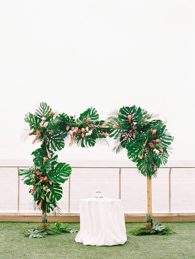 Hawaiian inspired wedding structure filled with greenery, tropical flowers and pineapple