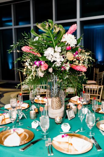 wedding reception set with teal linen, gold charger plates and tropical Hawaiian centerpieces