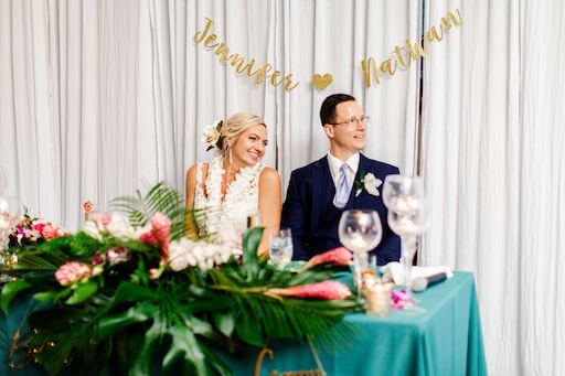 smiling newlyweds sitting at their Hawaiian inspired sweetheart table