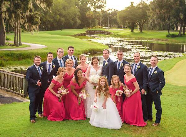 bride and groom posing for photos next to a lake with their large wedding party