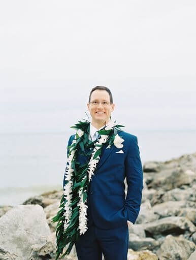 groom posing for photos on Clearwater Beach wearing a blue suit and traditional Hawaiian wedding lei