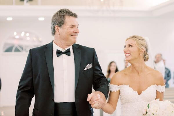 bride at harbor side chapel holding back tiers as she walks down the aisle with her father