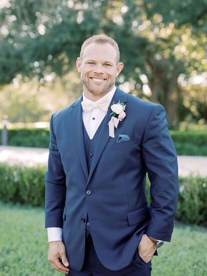 handsome groom wearing a navy blue three piece suit with white bow tie