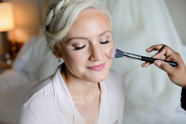 makeup artist applying blush to a beautiful bride