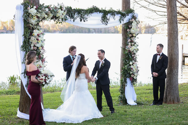 bride and groom holding hands as they exchange wedding vows surrounded by family and friends