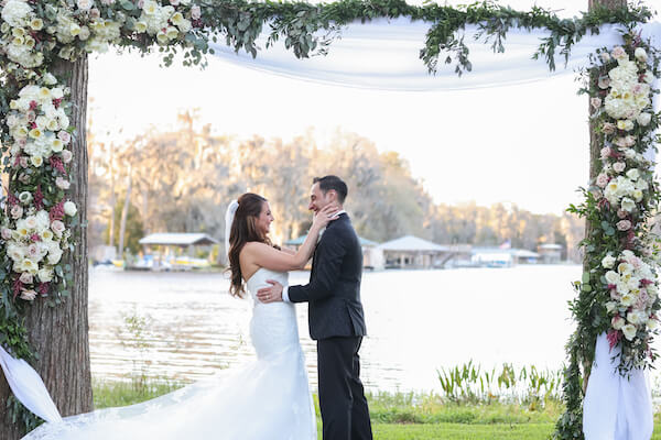 bride and groom posing for photos under their floral wedding arch