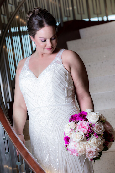 bride standing on the stairs of the Opal sands holding a pink ad purple bouquet with silver starfish