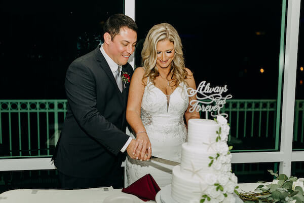 bride and groom cutting three-tiered white buttercream wedding cake with white buttercream flowers