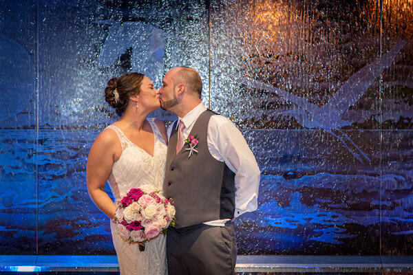 nighttime photo of a bride and groom kissing in front of the water feature at the Opal Sands Resort