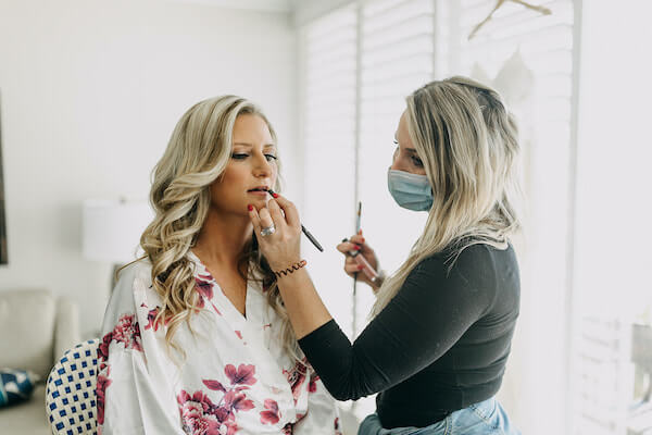 masked makeup artist touching up a bride's lipstick