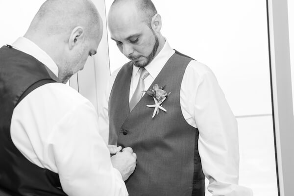 black and white photo of a groomsmen helping the from get dressed