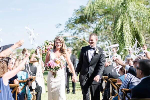 newlywed couple walking up the aisle as wedding guest wave ribbon wands