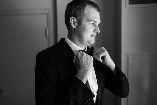 black and white photo of groom fixing his tie and getting dressed