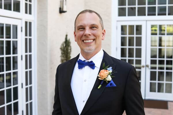 smiling groom wearing a bright blue bow tie and pockets square 