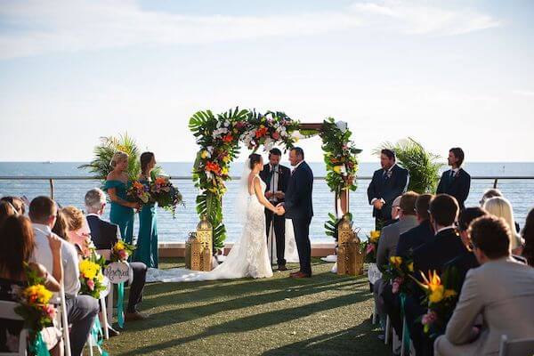 bride and groom exchanging wedding vows under a chuppah decorated with tropical flowers