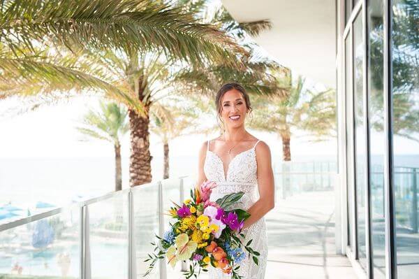 bride standing on the terrace at the Opal Sands Resort with a brightly colored bouquet of tropical flowers