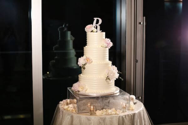 four tiered white buttercream wedding cake with pink flowers and' R' monogram cake topper