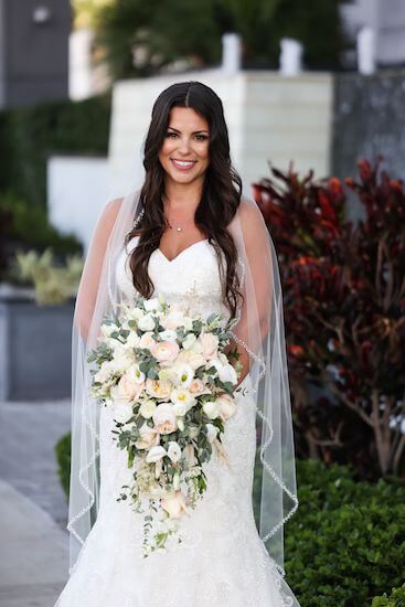 bride wearing a lace appliqué wedding gown with sweetheart neckline carrying a blush and white cascading bouquet