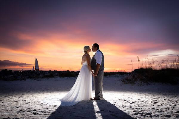 bride and groom kissing at sunset as a sail boat floats by