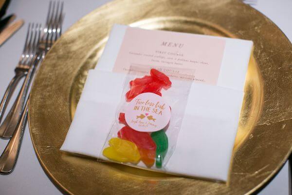 gold charger plate with a custom menu card and a wedding favor with Swedish fish for a beach themed wedding reception