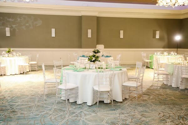 wedding reception set with white linen, clear acrylic chairs and runners and napkins in shades of sea foam and turquoise