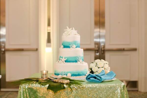 Three tiered ocean themed wedding cake on a shimmering green table cloth