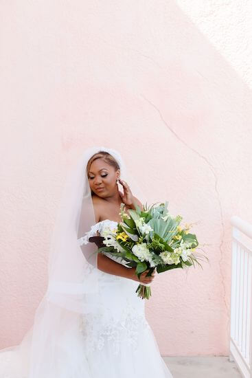 Beautiful curvy bride in a lace gown with long veil carrying a tropical bouquet with textured greenery