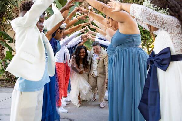 newlywed couple passing under an arch of their wedding parties arms