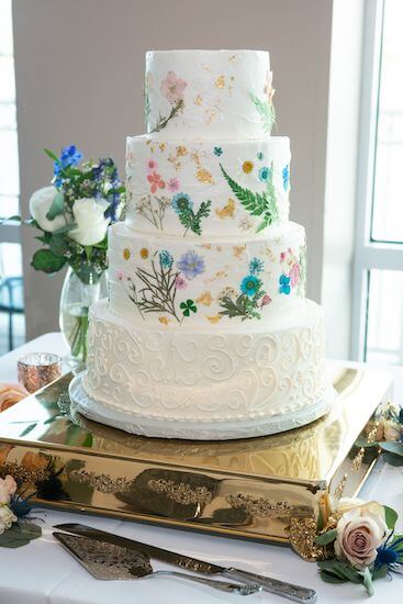 three tiered white wedding cake with pressed flowers